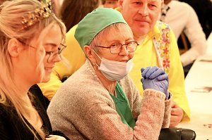 Karnevalsspektakel in einem gro&szlig;en Raum. Viele bunt gekleidete Menschen an Tischen und auf der B&uuml;hne