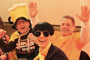 Karnevalsspektakel in einem gro&szlig;en Raum. Viele bunt gekleidete Menschen an Tischen und auf der B&uuml;hne