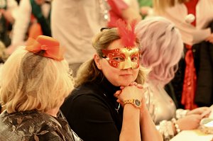 Karnevalsspektakel in einem gro&szlig;en Raum. Viele bunt gekleidete Menschen an Tischen und auf der B&uuml;hne