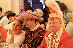 Karnevalsspektakel in einem gro&szlig;en Raum. Viele bunt gekleidete Menschen an Tischen und auf der B&uuml;hne