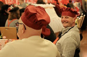 Karnevalsspektakel in einem gro&szlig;en Raum. Viele bunt gekleidete Menschen an Tischen und auf der B&uuml;hne