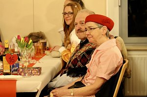 Karnevalsspektakel in einem gro&szlig;en Raum. Viele bunt gekleidete Menschen an Tischen und auf der B&uuml;hne