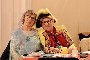 Karnevalsspektakel in einem gro&szlig;en Raum. Viele bunt gekleidete Menschen an Tischen und auf der B&uuml;hne
