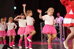 Karnevalsspektakel in einem gro&szlig;en Raum. Viele bunt gekleidete Menschen an Tischen und auf der B&uuml;hne