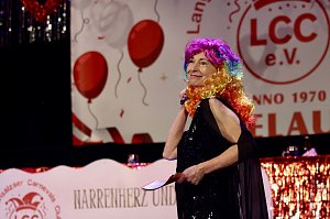 Karnevalsspektakel in einem gro&szlig;en Raum. Viele bunt gekleidete Menschen an Tischen und auf der B&uuml;hne