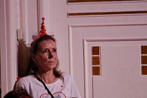 Karnevalsspektakel in einem gro&szlig;en Raum. Viele bunt gekleidete Menschen an Tischen und auf der B&uuml;hne