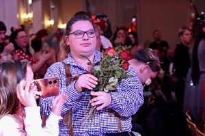 Karnevalsspektakel in einem gro&szlig;en Raum. Viele bunt gekleidete Menschen an Tischen und auf der B&uuml;hne