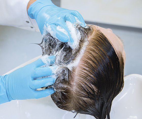 Bild: Eine Friseurin scheitelt das Haar der Probandin in der Mitte. Eine Seite w&auml;scht sie mit dem Stan&shy;dard-Shampoo, die andere mit einem Test&shy;produkt.