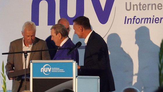 Bild: NUV-Ehrenpr&auml;sident Hans-Joachim Junker &uuml;berreichte Schr&ouml;der eine Flasche Doppelkorn einer limitierten Edition.