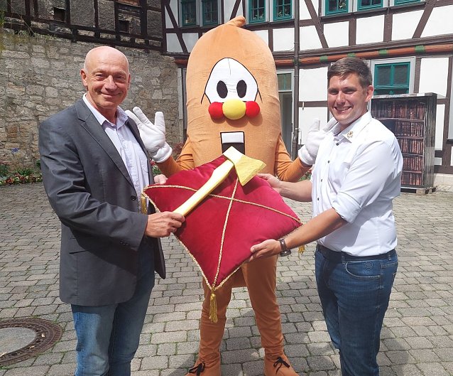 Bild: Markus Edom vom Kultur-Referat der Stadt M&uuml;hlhausen, Maskottchen Wurschti und der Betriebsleiter des Bratwurstmuseums, Kay Wipprecht, mit der Goldenen Axt, die bei den traditionellen Wettbewerben zur Holzfahrt am Samstag in mehreren Kategorien verliehen wird