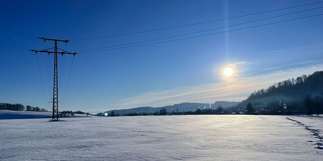 Bild: Ein Hochspannungsmast steht in einer verschneiten Landschaft. 