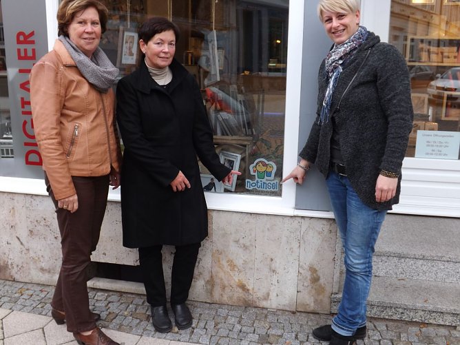 Katja Klaus, Regina Haupt und Birgit Schmidt (v. r.) pr&auml;sentieren das Notinsel-Logo im Schaufenster des Fotogesch&auml;fts am Frauentor in M&uuml;hlhausen.  (Foto: Foto: Mix)
