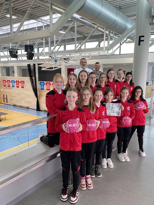 Tobias Ernst (stellv. Vorsitzender des Vereins) (h.r.) und Andrej Minewski (Trainer der D-Jugend) (h.l.) zusammen mit den M&auml;dchen der D- und E-Jugend des THC bei der symbolischen Scheck&uuml;bergabe (Foto: Landratsamt UHK)